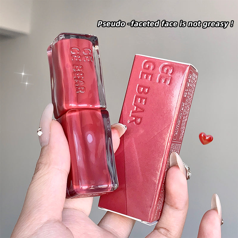 Red lip gloss with packaging held by a hand, on a neutral background