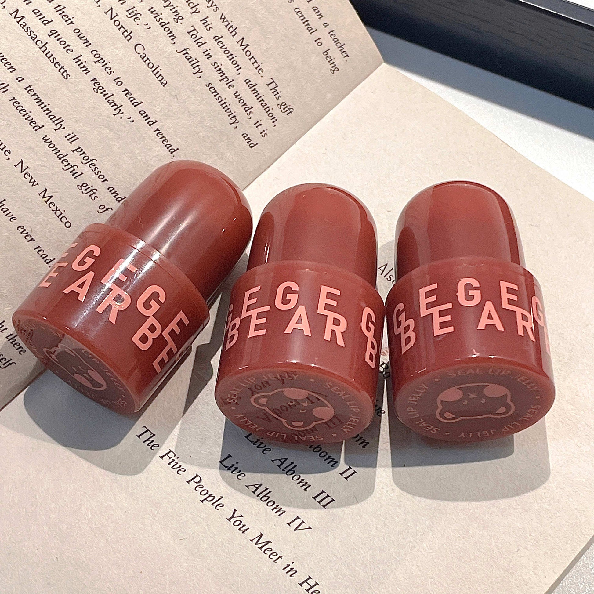 Three red lip balm tubes with 'GEGE BEAR' branding on a surface with text.