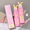 Two pink and yellow lip balms with bunny designs held by a hand, next to their packaging.