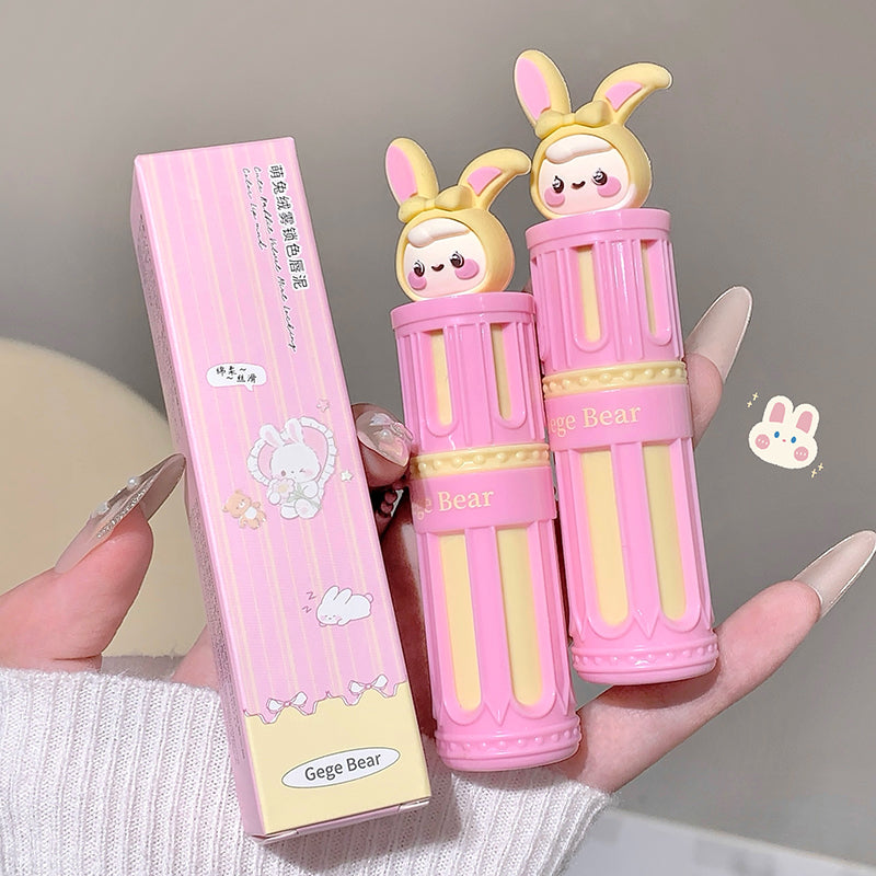 Two pink and yellow lip balms with bunny designs held by a hand, next to their packaging.