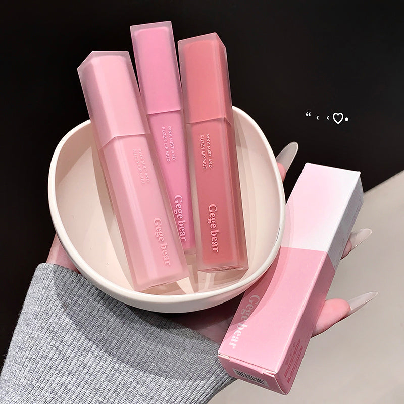 Pink lip glosses in a bowl with one outside on a gray surface