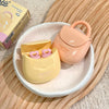 Two small bags, one yellow and one pink, on a white plate with a wooden surface underneath.