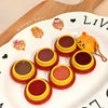 Set of small round containers with yellow and red lids on a white surface with cartoon bear illustrations.