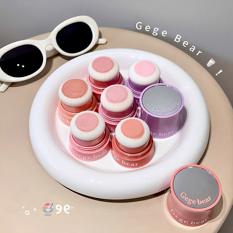 Set of pink and gray cosmetic products with 'Gege Bear' branding on a white tray, accompanied by white sunglasses.