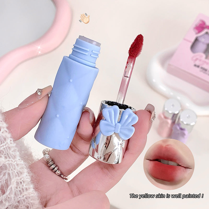 Blue lip gloss with a bow design held by a hand, with close-up of lips and product inset.