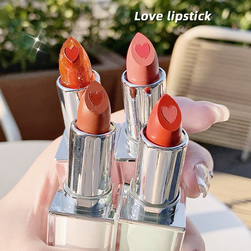 Four lipsticks with heart designs on a reflective surface outdoors.