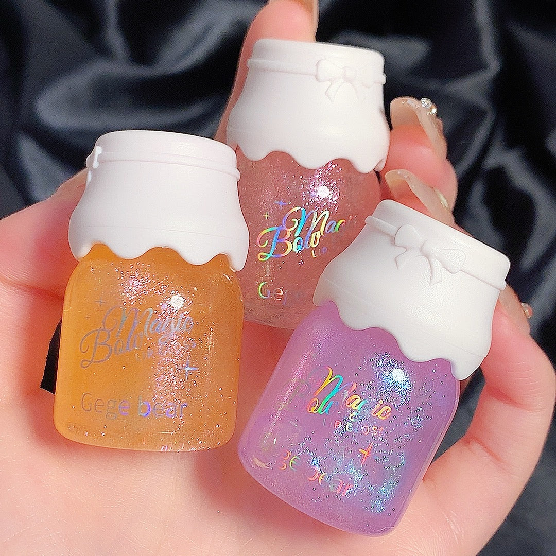 Three small bottles of nail polish with colorful glittery contents held in a hand against a dark satin background.