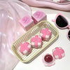 Pink cosmetic products with a bow design on a white surface, including a small basket and sunglasses.