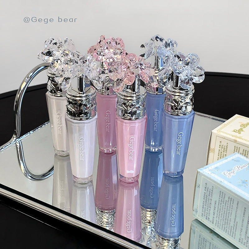 Set of lip glosses with decorative tops on a reflective surface.