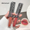 Two lip glosses in packaging held by a hand, with a close-up of a mouth wearing the product.