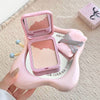 Pink makeup compact held by a hand on a textured surface