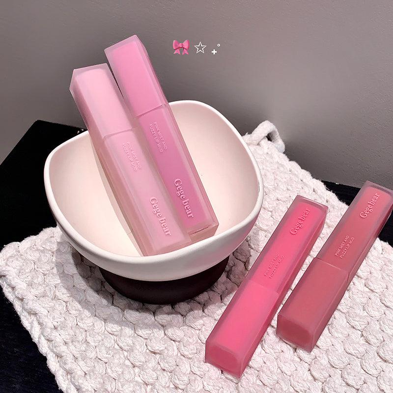 Pink lip glosses with a bowl on a textured surface