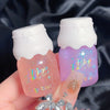 Two lip gloss containers with colorful text on a dark fabric background