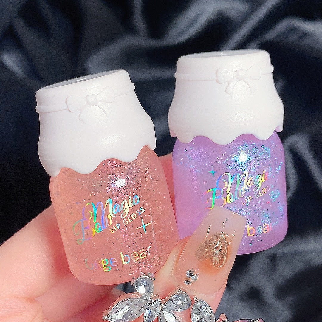 Two lip gloss containers with colorful text on a dark fabric background