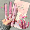 Pink lip gloss with cartoon packaging held by a hand, on a gray background.