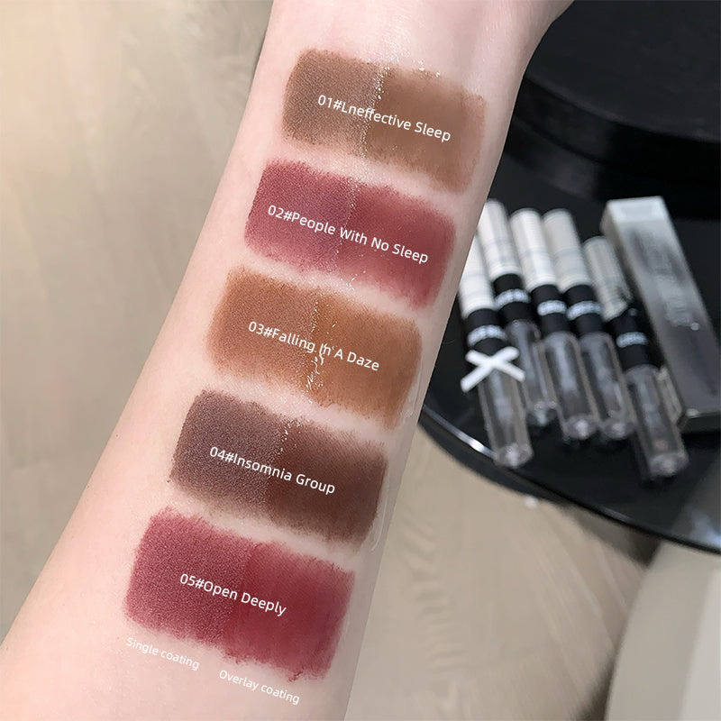 Lipstick swatches on a person's arm with labeled colors and a set of lipsticks in the background.