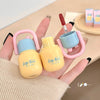 Two small yellow bottles with pink handles held by a hand on a light background