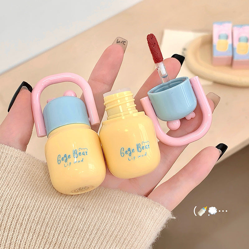 Two small yellow bottles with pink handles held by a hand on a light background