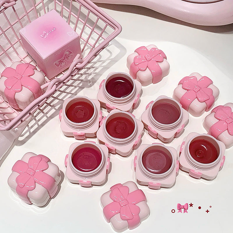 Pink lip balm containers with red lip balms on a white surface, with a pink shopping cart in the background.