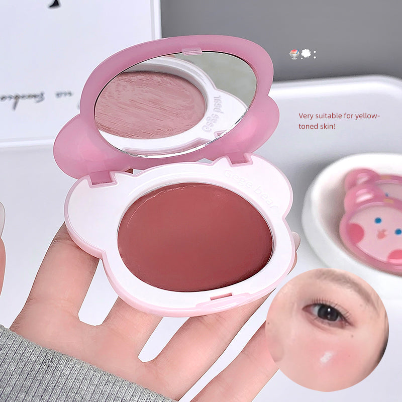 Compact blush with mirror and pink bunny design held by a hand, with close-up of blush on skin.