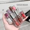 Hand holding six lipsticks with metallic caps, displayed against a blurred background with 'GEGE BEAR' branding.