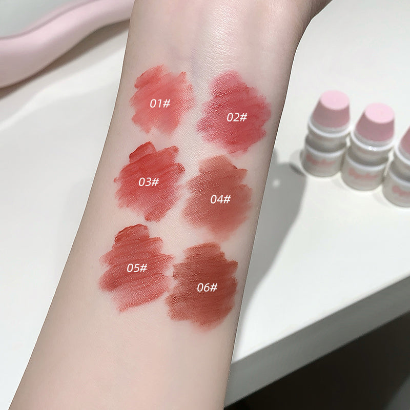 Lipstick swatches on a person's arm with labeled colors, next to lipsticks in small containers.