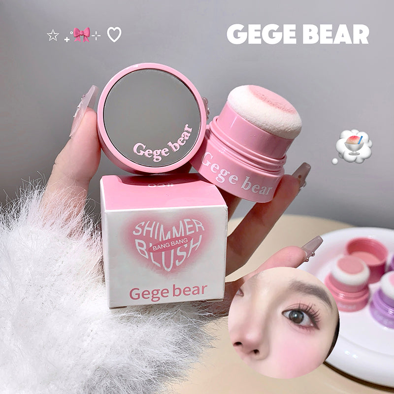 Pink makeup product with 'Gege Bear' branding held by a hand, with packaging and blurred face in the background.