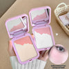 Pink makeup compact with mirror held by a hand, on a beige background.