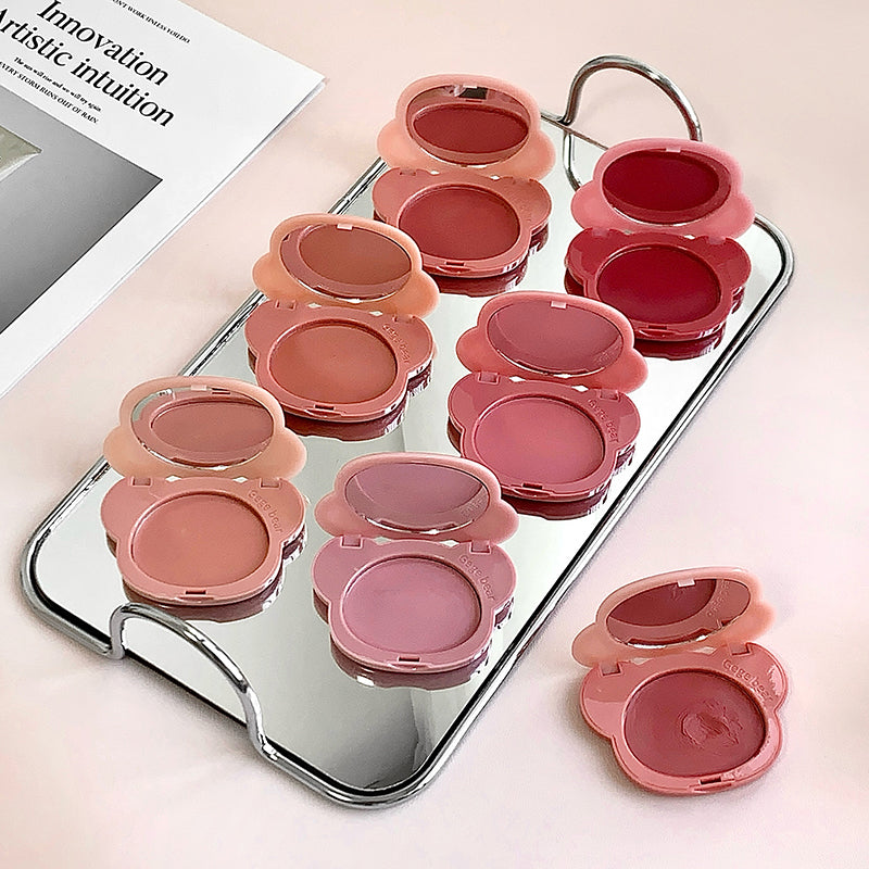Set of pink lip glosses in open and closed positions on a mirror with a magazine in the background.
