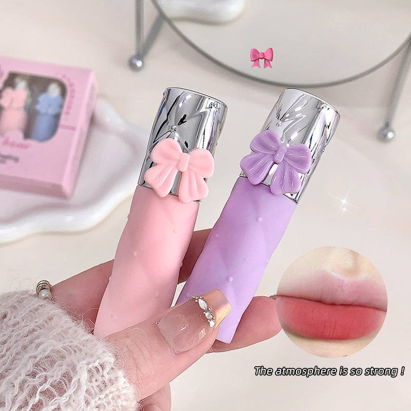 Pink and purple lip glosses with butterfly designs held by a hand, close-up view.