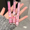 Three pink makeup pencils with cartoon designs held in a hand against a neutral background
