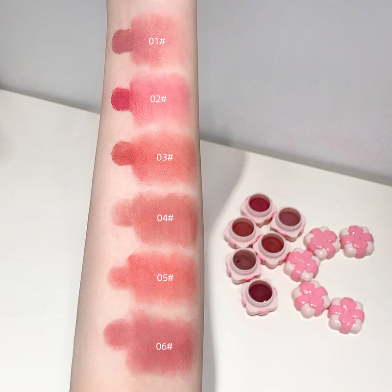 Lipstick swatches on an arm with six different shades and a set of lipsticks in pink cases.