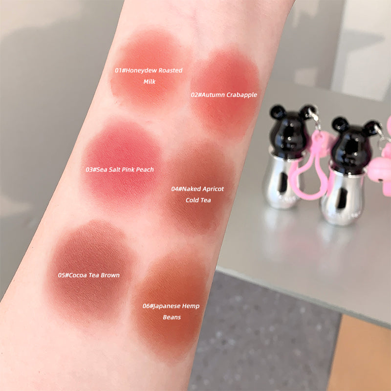 Lip color swatches on a wrist with product names labeled, set against a neutral background.