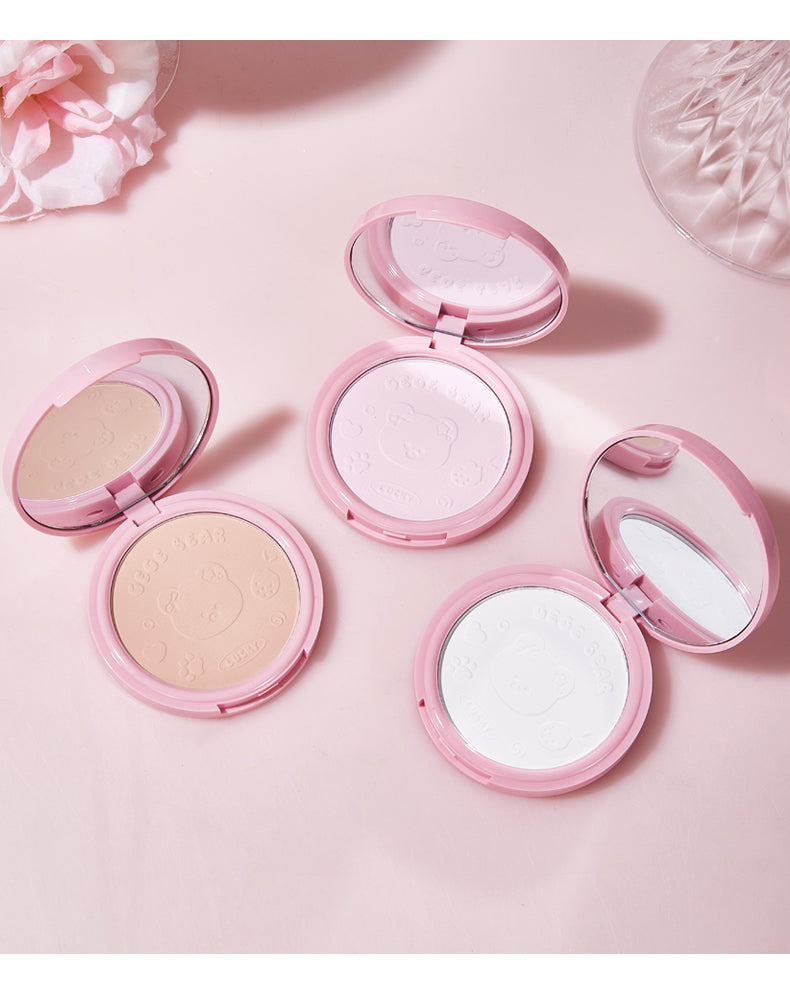 Four pink makeup compacts with different powders on a light pink background