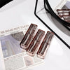 Three transparent lip glosses on a newspaper with a mirror and pink items in the background.