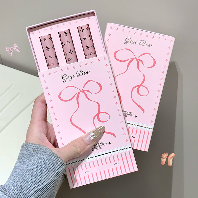 Pink lip gloss set with 'Gaze Bear' branding held by a hand on a light gray background.