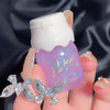 Hand holding a small purple bottle with a white cap against a dark fabric background