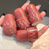 Close-up of George Bear lip balm tubes held by a hand on a textured surface.