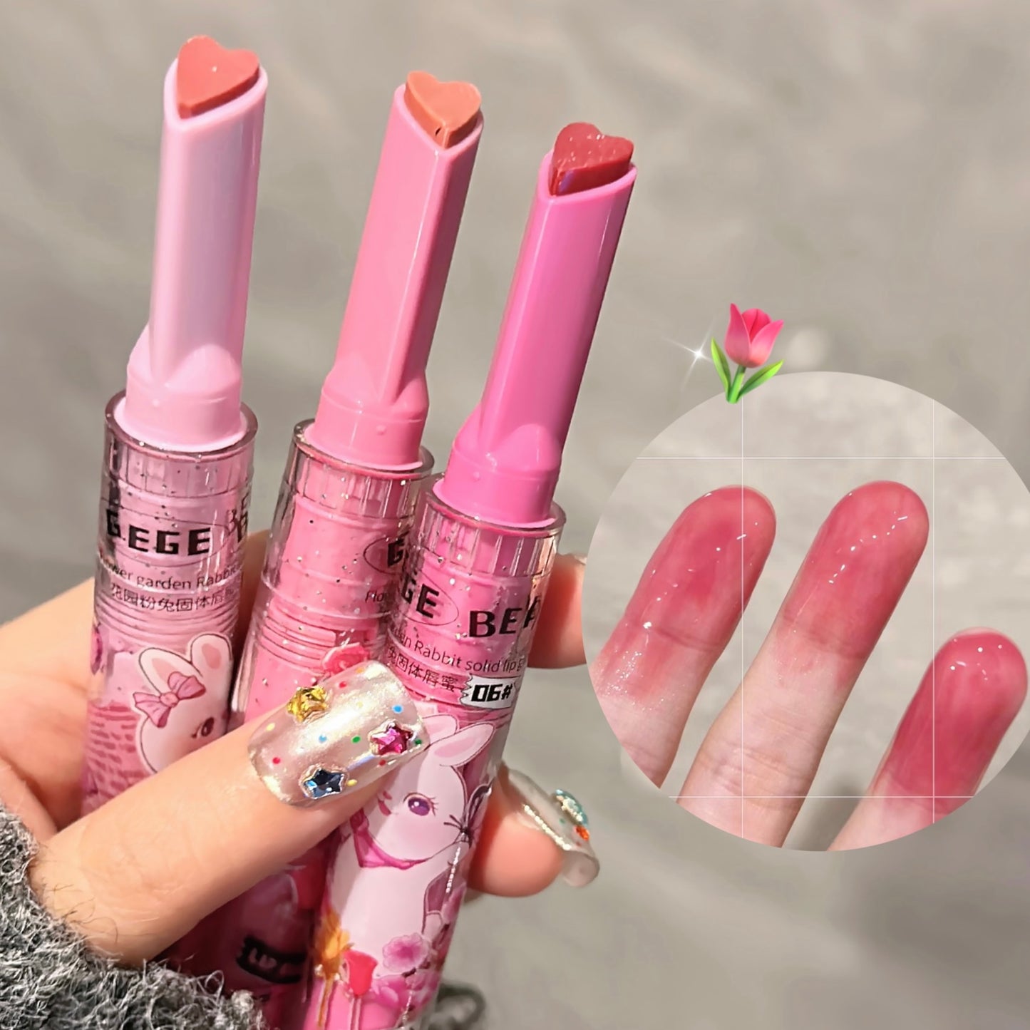 Three pink lip balms held by a hand with colorful nail art, inset showing matching lip color on skin.