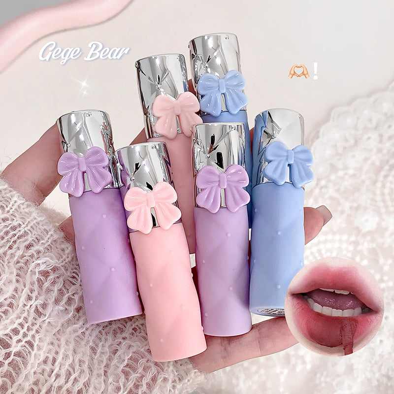 Set of colorful lip glosses with bow accents held by a hand, on a textured white background.