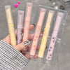 Set of lip glosses in clear packaging held by a hand with striped sleeves.