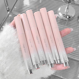 Set of gradient pink lip glosses held by a hand on a reflective surface.