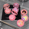 Pink makeup compact cases with cartoon designs on a reflective surface