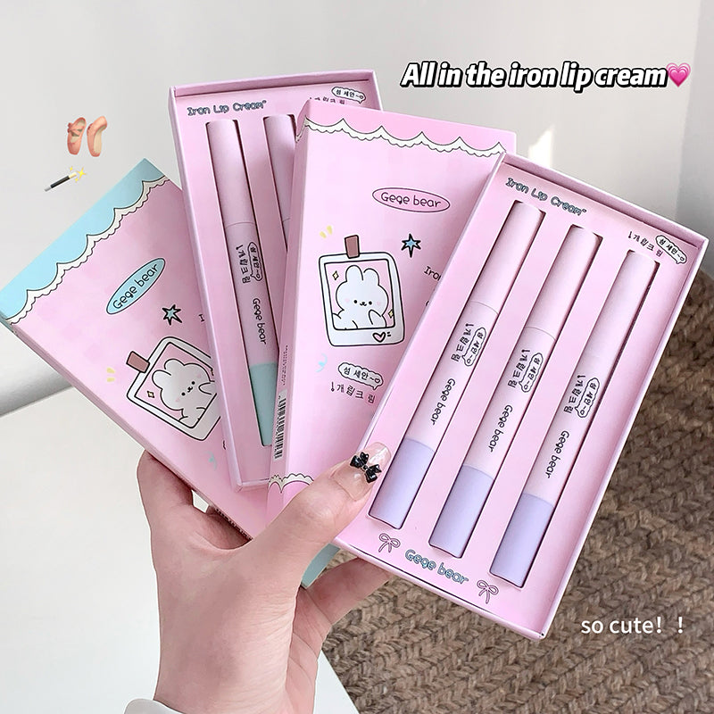 Set of pink lip cream products with a hand holding them, on a neutral background.