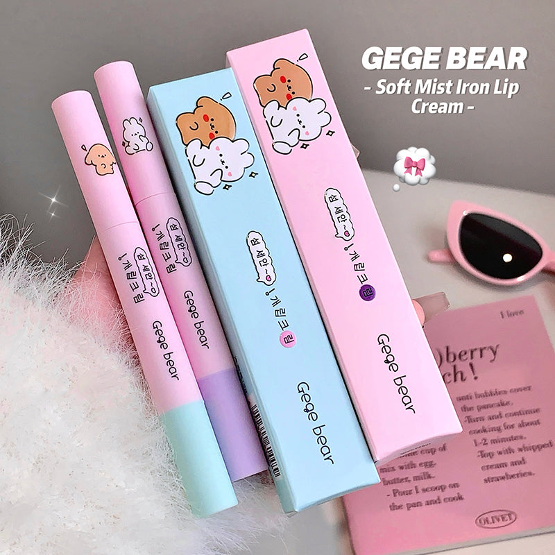 Three 'GEGE BEAR' soft mist iron lip cream packaging on a soft surface with a pink cup in the background.
