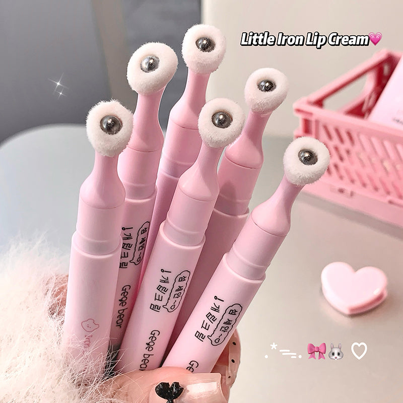 Pink lip cream with white applicators held by a hand, with a pink heart and basket in the background.
