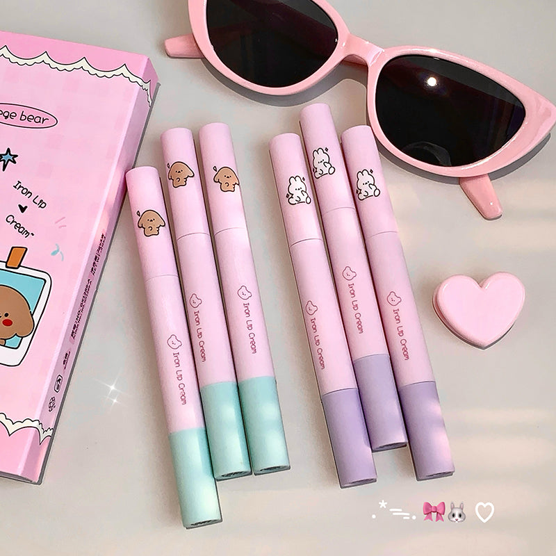 Set of pink lip glosses with a heart-shaped container and sunglasses on a light background