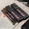 Three 'GEGE BEAR' mascara tubes with their packaging held by a hand on a neutral background.