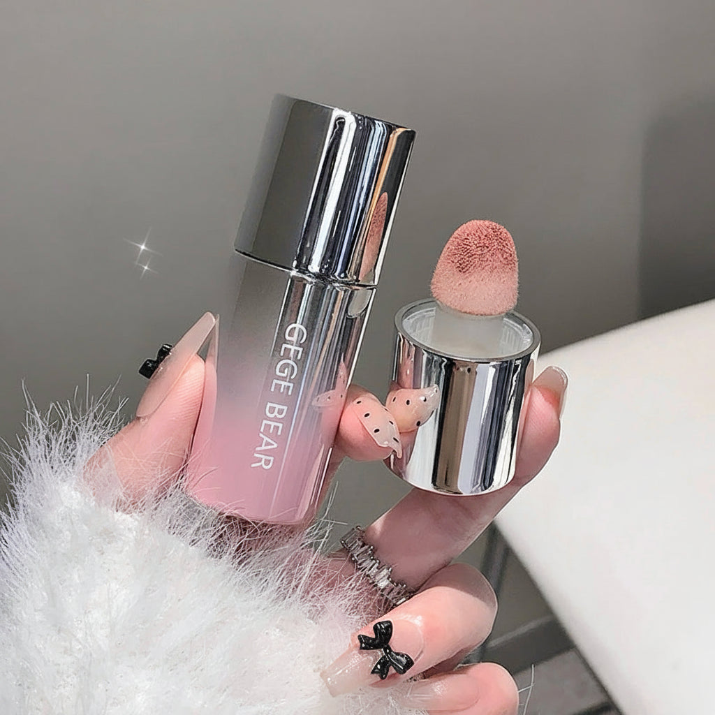Makeup product with pink cap and silver body held by a hand on a neutral background