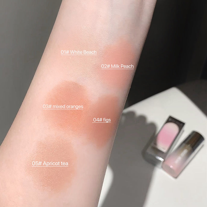 Color swatches on a person's arm with labeled shades and a small makeup product in the background.